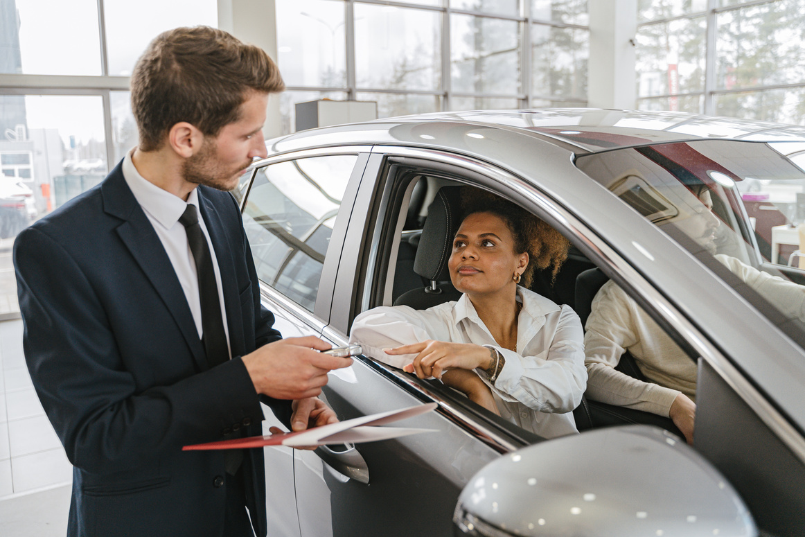 Car Dealer Handing in Keys to a Woman Sitting in a New Car 